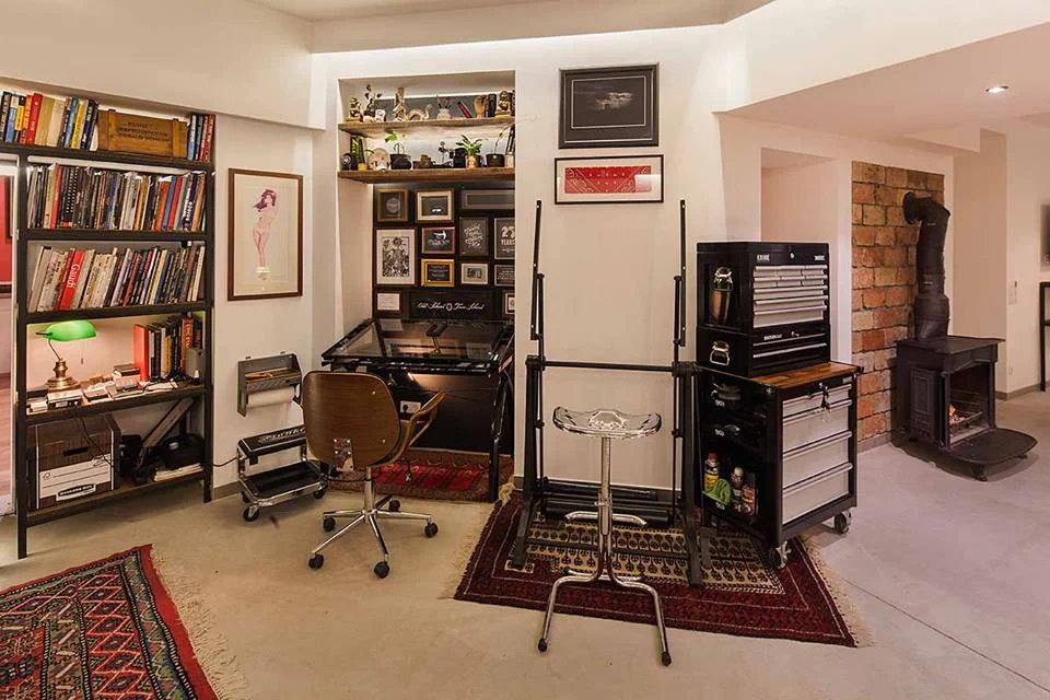 Werkstatt-Ecke der John Ross Group: Zeichentisch, Bücherregal mit grüner Lampe, Werkzeugwagen und Ofen